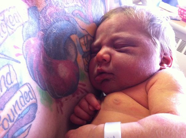 Baby resting on tattooed parent's chest, highlighting their bond.