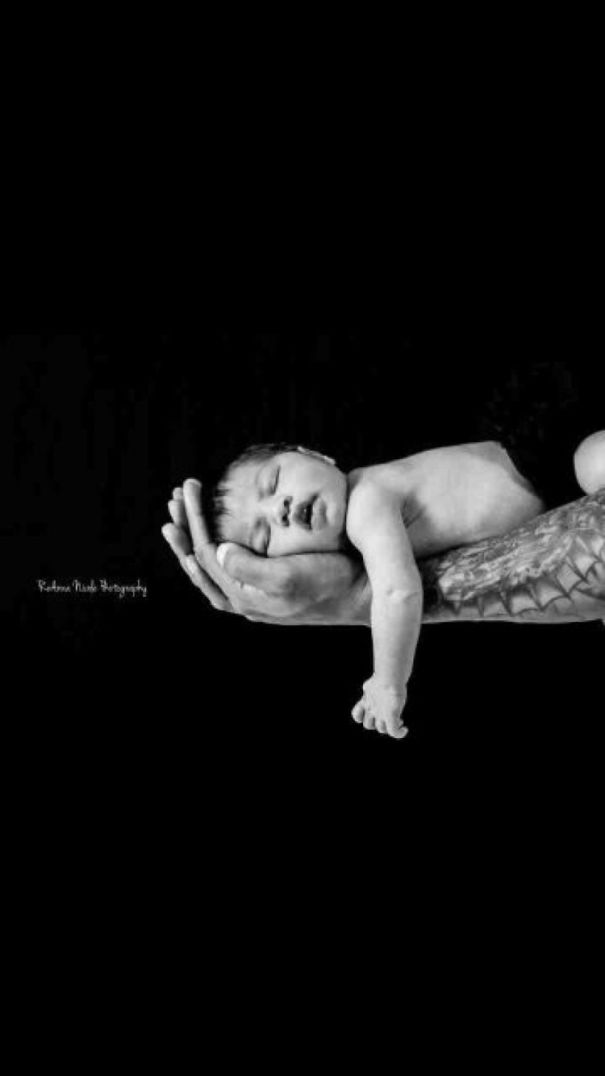 Baby sleeping peacefully in tattooed parent's hand, showcasing a beautiful connection.