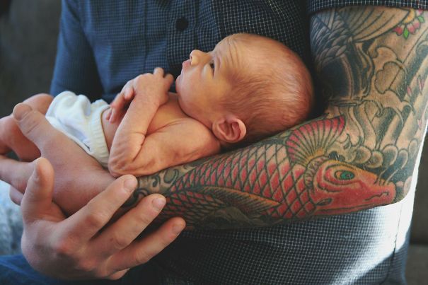 Tattooed parent holding a newborn baby, showcasing beautiful contrast between tattoos and the baby's delicate skin.
