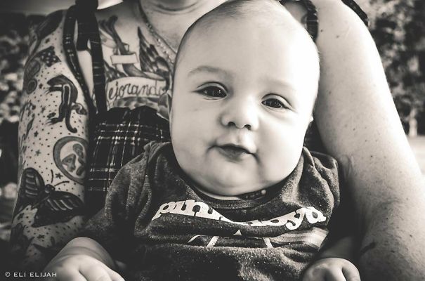 Baby in the arms of a tattooed parent, both looking content and beautiful together.