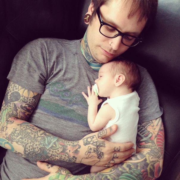 Tattooed parent cradling a baby peacefully on a couch.