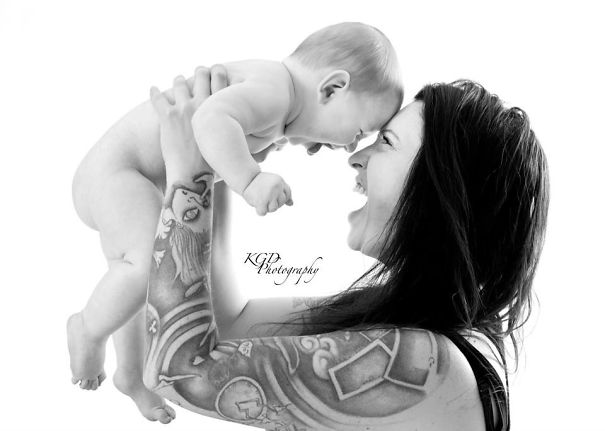 Tattooed parent joyfully lifting baby, showcasing their bond and unique tattoos.