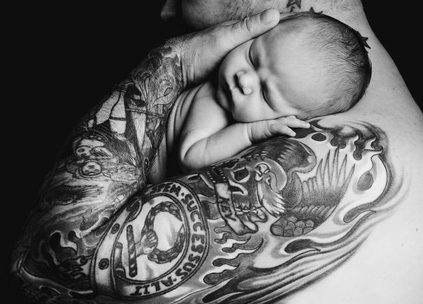 Tattooed parent gently holding a sleeping baby, showcasing a beautiful connection between tattoos and parenthood.