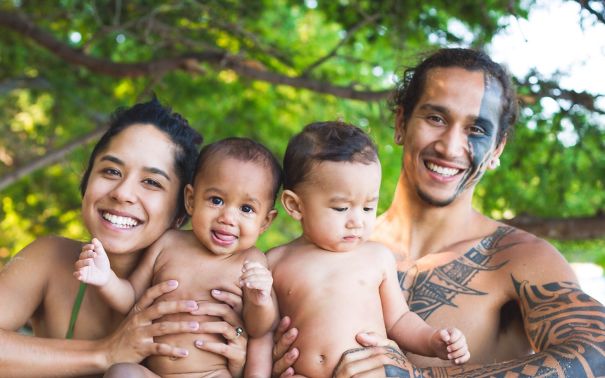 Tattooed parents smiling with their two babies outdoors, showing family beauty and happiness.