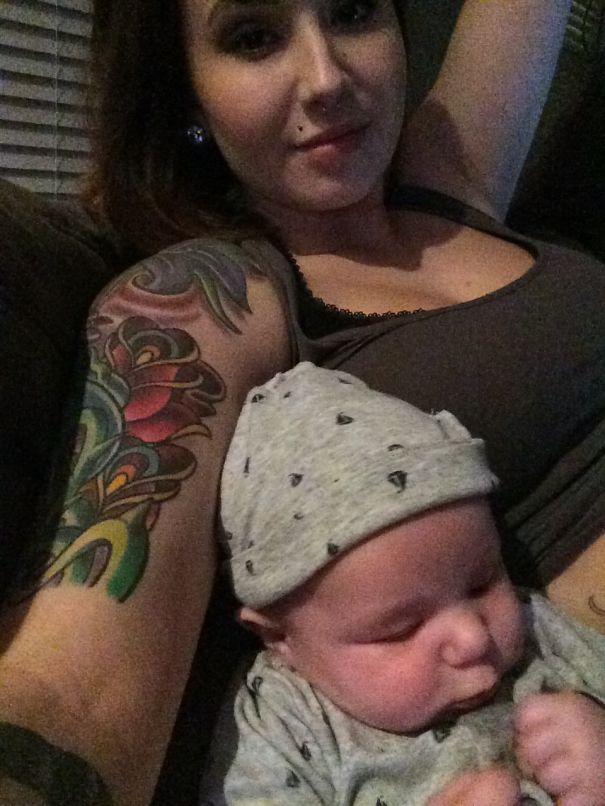 Tattooed parent lying with baby on couch, colorful arm tattoo visible.