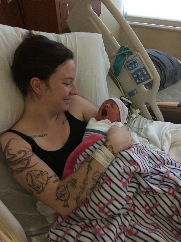 Tattooed parent lovingly holding their newborn baby in a hospital bed, surrounded by soft blankets.