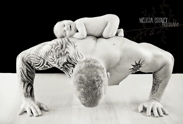 Tattooed parent doing push-up with baby on back, showcasing beautiful bond.