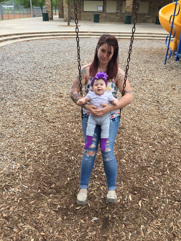 Tattooed parent swings with baby in park, showcasing beautiful bond and tattoos.