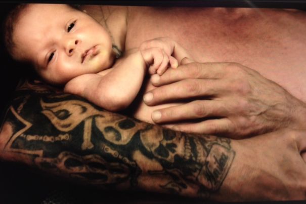 A baby resting on a tattooed parent's arm, showcasing the contrast between soft skin and detailed body art.