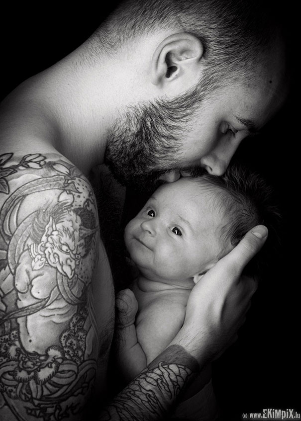 Tattooed parent gently holding a smiling baby, showcasing their bond and contrasting body art.
