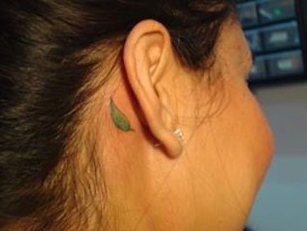 Ear tattoo featuring a small green leaf design behind the ear.