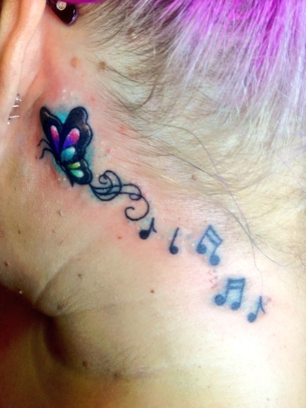Colorful butterfly and music notes ear tattoo with purple hair.
