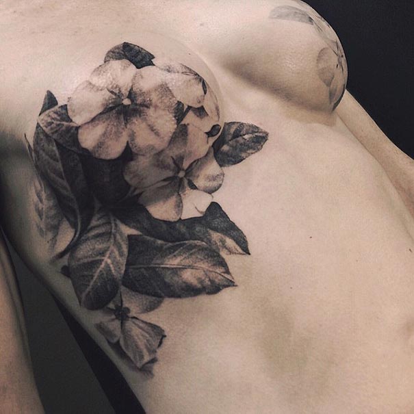 A detailed black-and-gray floral tattoo on the chest area, featuring realistic flowers and leaves blending seamlessly with the skin.