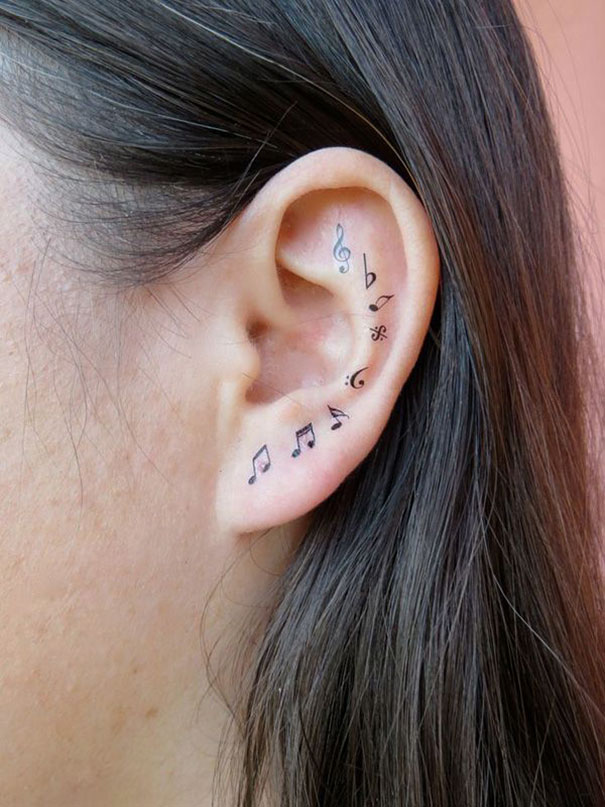 Creative ear tattoo with musical notes and symbols on the inner ear.