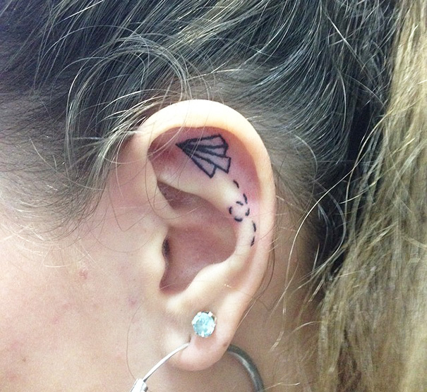 Creative ear tattoo of a paper airplane on the inner ear with a gem earring below.