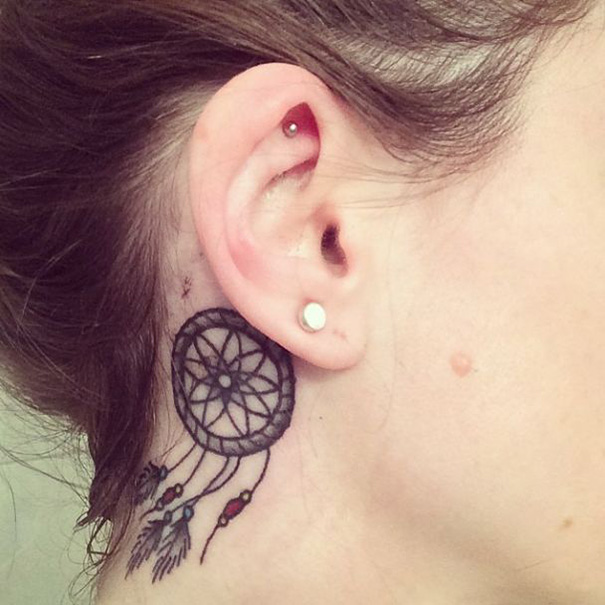 Creative ear tattoo of a dreamcatcher behind the ear with small details and colorful beads.