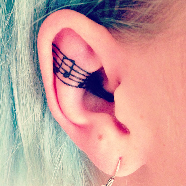 Creative ear tattoo featuring musical notes blended with teal hair.