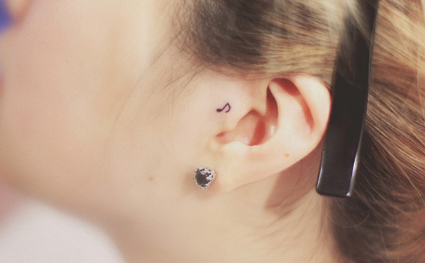 A small creative ear tattoo of a musical note behind the ear.