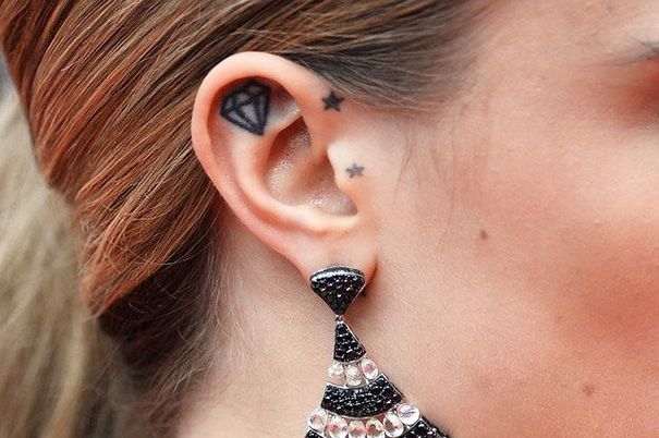 Ear with creative tattoos featuring a diamond and stars, adorned with a sparkling earring.