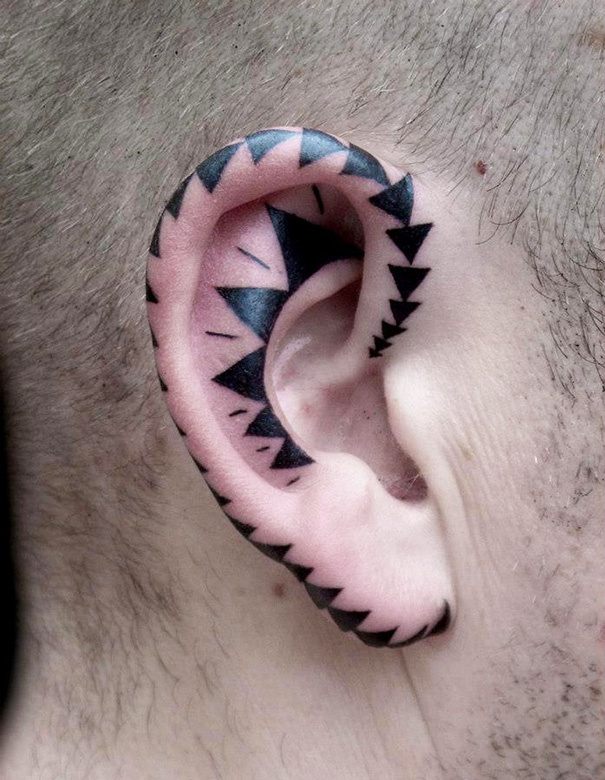 Creative ear tattoo with black triangles forming a pattern along the ear's edge.