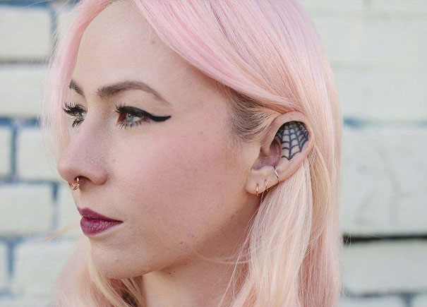 Woman with pink hair and spider web ear tattoo, showcasing creative ear design.