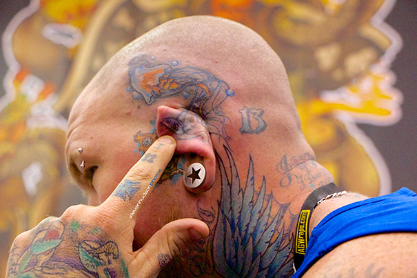 Creative ear tattoo featuring blue wings and colorful designs on a person's head and neck.