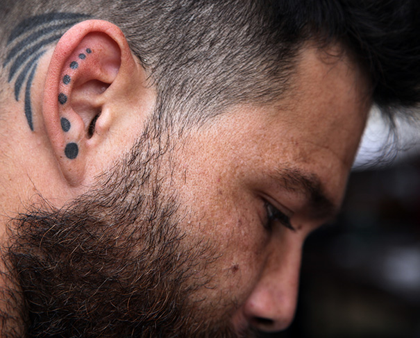 Man with creative ear tattoo featuring black dots and lines.