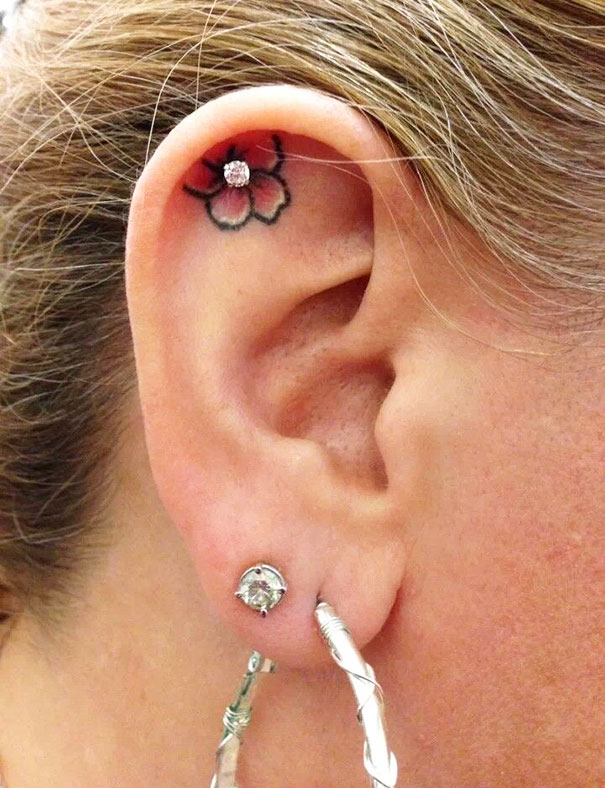 Creative ear tattoo featuring a delicate pink flower with gemstone, adorned with hoop earrings.
