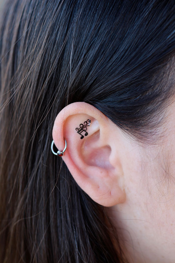 Creative ear tattoo with a musical note design and hoop earring.