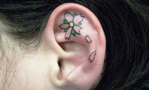 Ear tattoo with a pink flower design on the inner part of the ear.