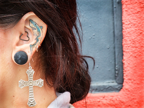 Creative ear tattoo featuring a shark design, complemented by heart-shaped and cross earrings.