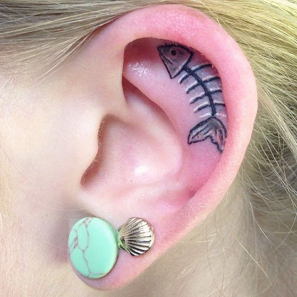 Creative ear tattoo of a fish skeleton with a green and shell earring.