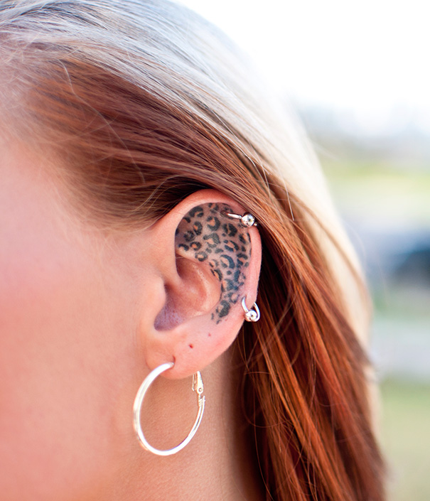 Creative ear tattoo with leopard print design and multiple piercings.