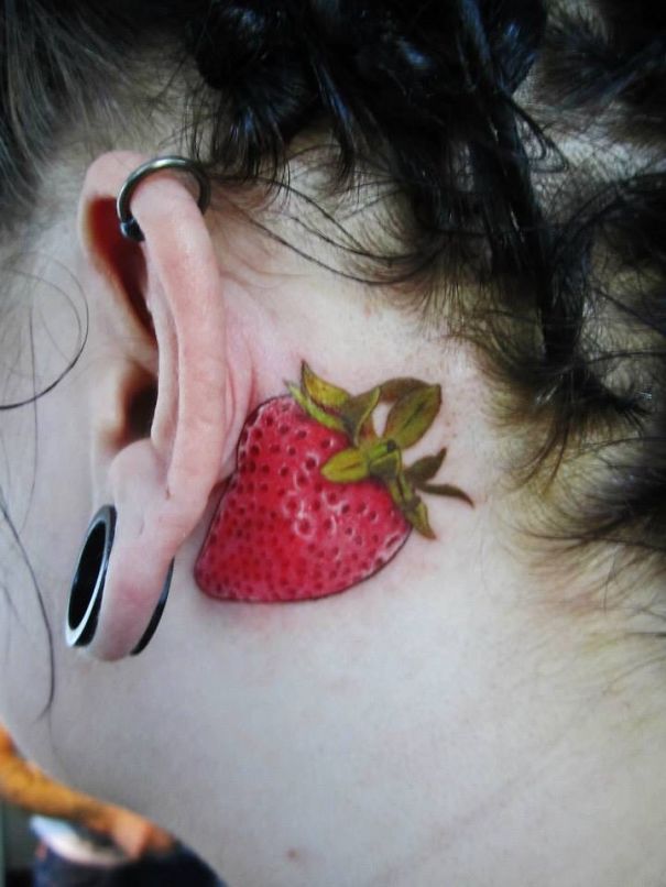 Creative ear tattoo with a vibrant strawberry design behind the ear.