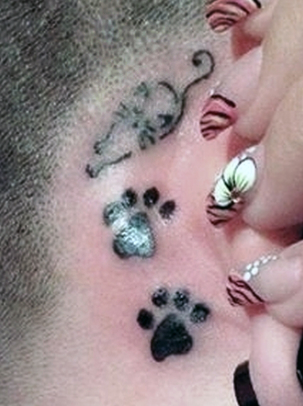 Simple line art cat tattoo with paw prints behind the ear.