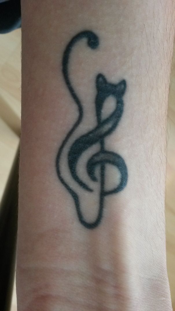Line art tattoo of a cat and treble clef on forearm, perfect for cat lovers seeking simple designs.