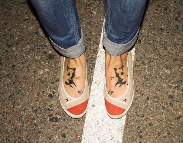 Feet with cat line art tattoos wearing casual shoes and jeans.
