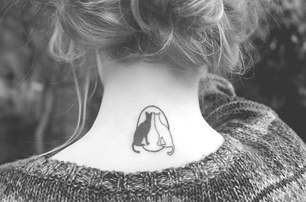 Line art cat tattoo on the back of a woman's neck, featuring two cats in a simple design.