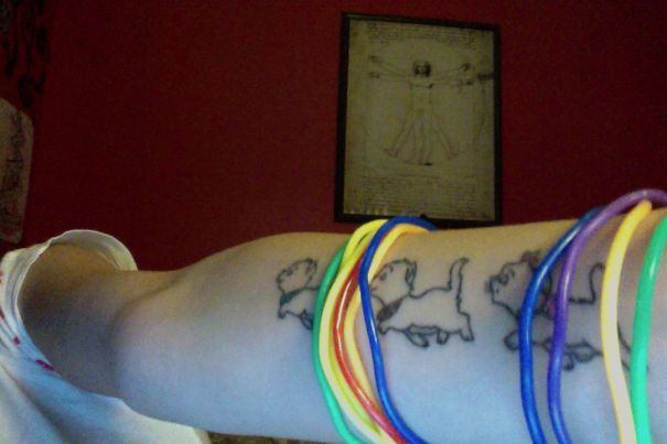 Arm with simple cat tattoos in line art style, adorned with colorful bracelets.