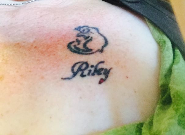 Minimalist cat line art tattoo with name "Riley" beneath it.
