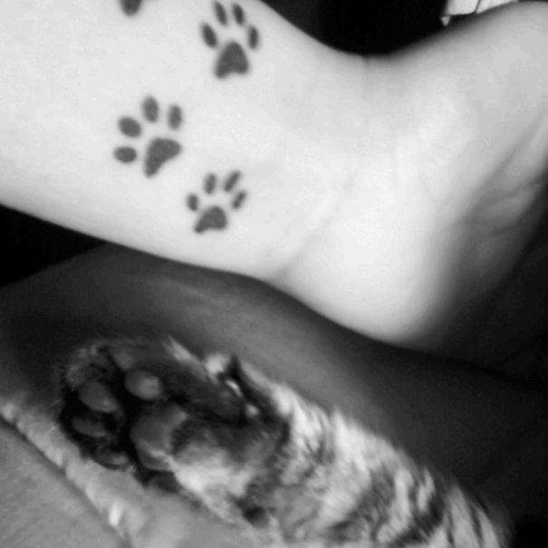 Simple cat tattoo with paw prints on arm, alongside a cat’s paw, in a black and white line art style.