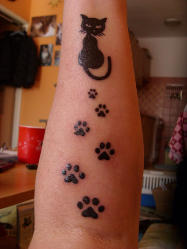 Line art cat tattoo design with paw prints on forearm.
