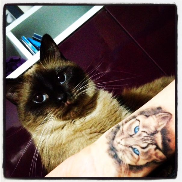 A simple cat tattoo design on a wrist next to a real cat, showcasing line art for cat lovers.