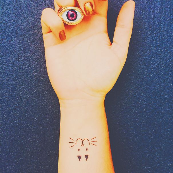 Minimalist cat tattoo design on forearm with an eye-shaped ring, perfect for cat lovers and line art enthusiasts.