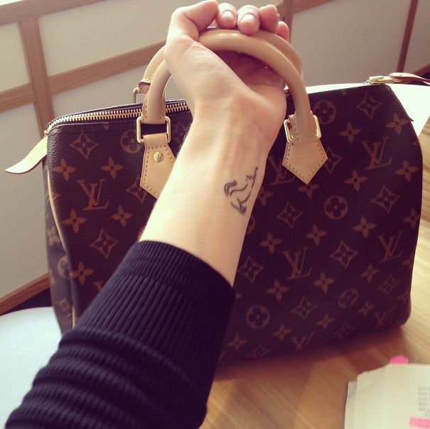 Simple cat tattoo design on a person's wrist, holding a designer handbag.