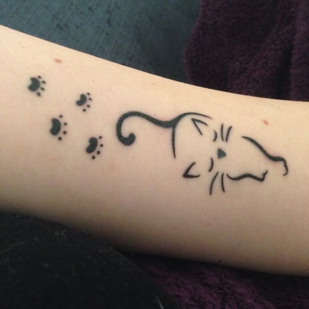 Simple cat tattoo design featuring cat face and small paw prints on arm.