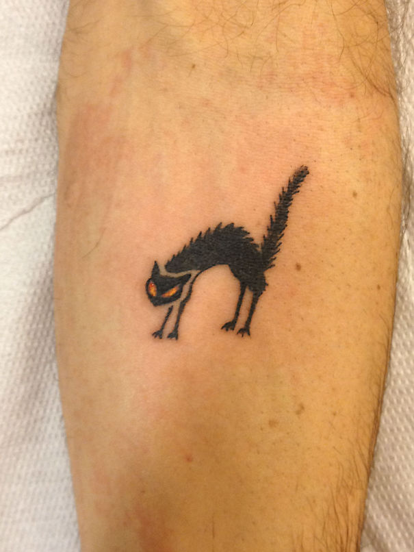 Simple cat tattoo design featuring a stretching black cat with orange eyes on an arm.