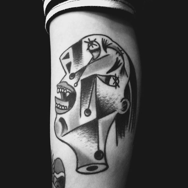 Picasso-inspired tattoo design in black ink on forearm, featuring abstract facial elements and geometric shapes.