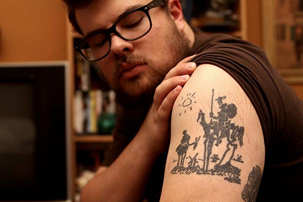 Man showcasing Picasso-inspired tattoo on his arm featuring abstract figures and a sun.