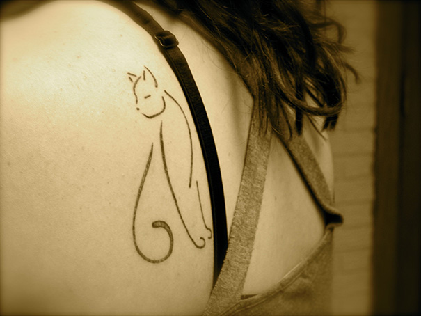 Line art cat tattoo on woman's shoulder, showcasing simple cat designs for cat lovers.